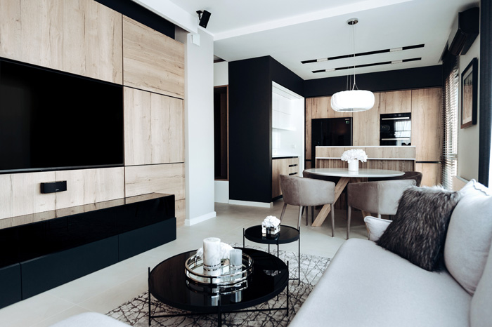 Modny i nowoczesny salon w 50 metrowym mieszkaniu. Salon w kolorach czerni, szarości i naturalnego drewna. Wzbogacony o szklane dodatki takie jak nowoczesne stoliki Cupid Zuiver
